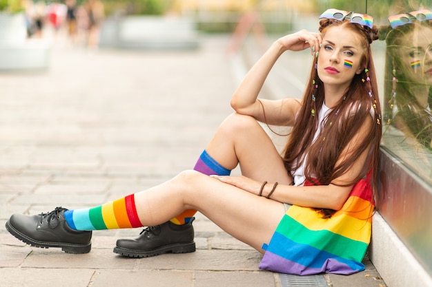 Modelo lésbica elegante com bandeira lgbt no rosto posando ao ar livre.