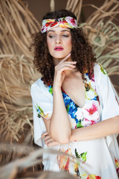 Una modelo lleva un vestido floreado con una diadema floral y un pañuelo blanco.