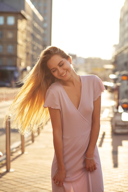 Modelo loira alegre com cabelo comprido posando na avenida em um raio de sol