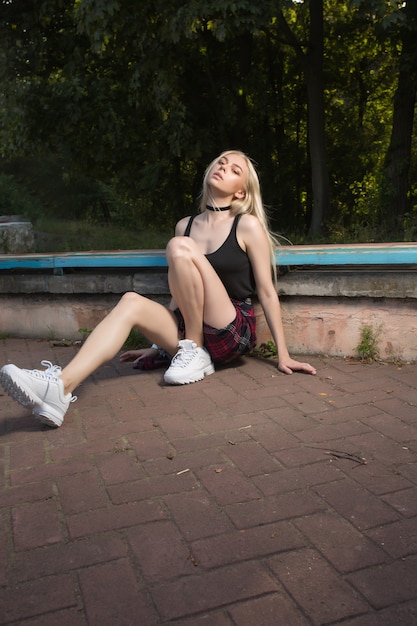 Modelo loira bonita em roupas casuais posando em um banco do parque