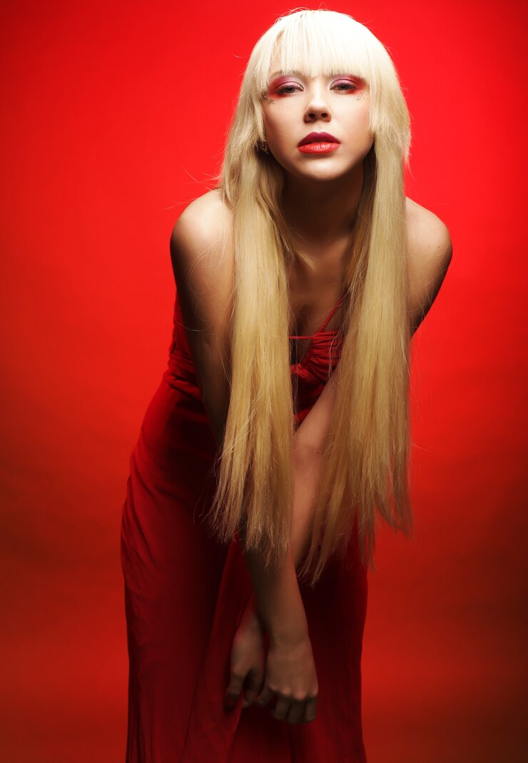 Foto modelo loiro perfeito em um vestido vermelho sobre uma parede vermelha. maquiagem de fantasia.