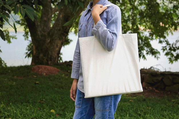 Foto modelo mantenga la bolsa de tela blanca en blanco para salvar el medio ambiente en el parque