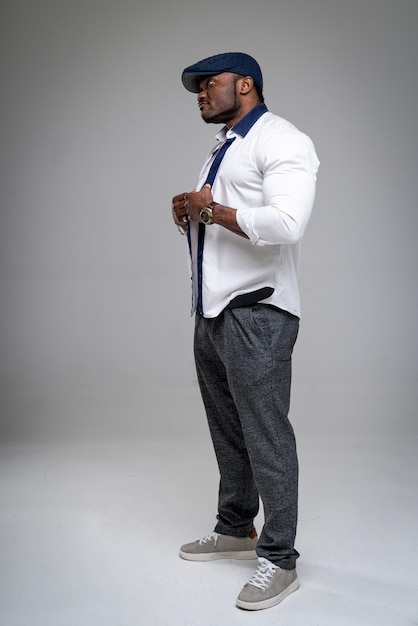 Modelo masculino afroamericano joven sonriente de aspecto natural aislado en fondo gris. Hombre de moda con camisa blanca y gorra azul. De cerca.