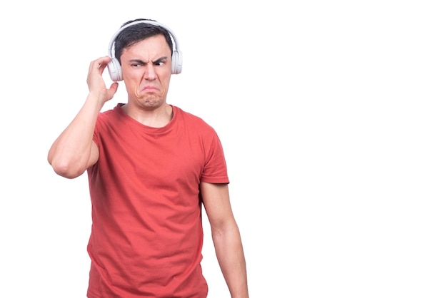 Modelo masculino aislado en camiseta roja tocando auriculares insatisfechos con la música sobre fondo blanco