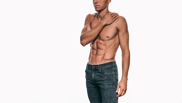 Foto modelo masculino atlético en jeans mostrando su cuerpo sexy aislado en un fondo blanco hombre culturista sin camisa con abdomen sexy posando sobre pared blanca deporte de salud y concepto de personas