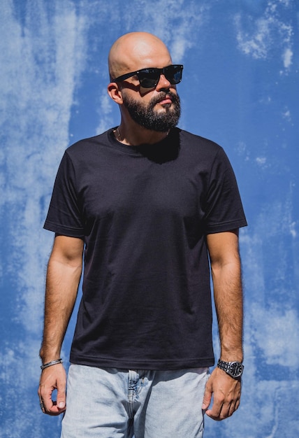 Modelo masculino con barba con camiseta negra en blanco en el fondo de una pared azul