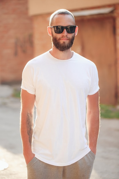 Modelo masculino bonito hipster com barba usando uma camiseta branca em branco com espaço para seu logotipo ou desenho em estilo urbano casual