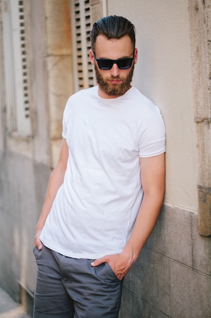 Modelo masculino bonito hipster com barba usando uma camiseta branca em branco com espaço para seu logotipo ou desenho em estilo urbano casual