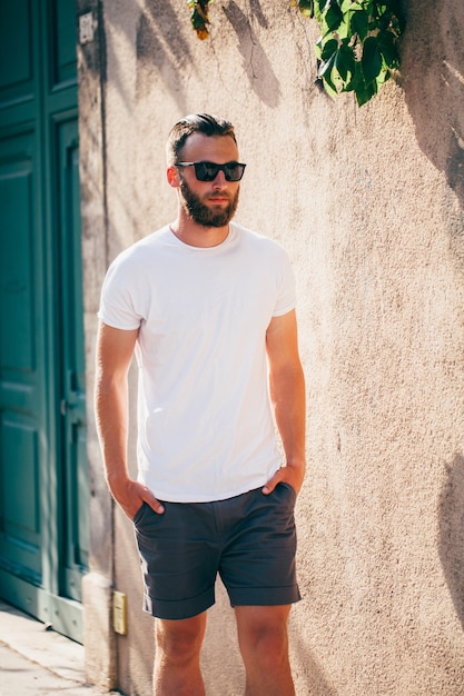 Modelo masculino bonito hipster com barba usando uma camiseta branca em branco com espaço para seu logotipo ou desenho em estilo urbano casual