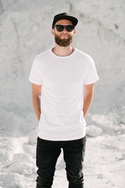 Modelo masculino bonito hipster com barba usando uma camiseta branca em branco e um boné de beisebol com espaço para seu logotipo ou desenho em estilo urbano casual