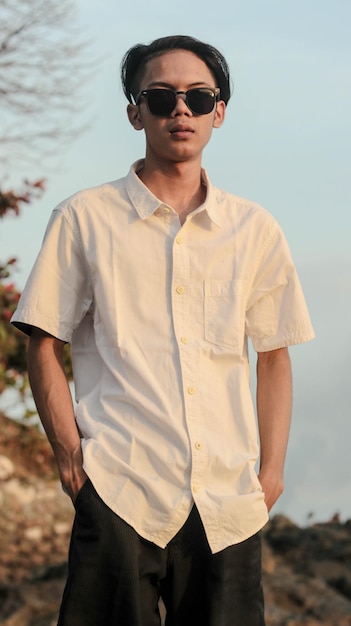 modelo masculino em pé de camisa branca na praia com belo pôr do sol