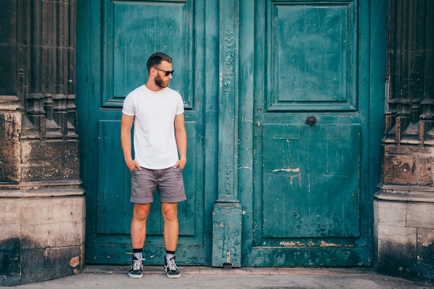 Modelo masculino guapo hipster con barba con camiseta blanca en blanco con espacio para su logotipo o diseño en estilo urbano casual