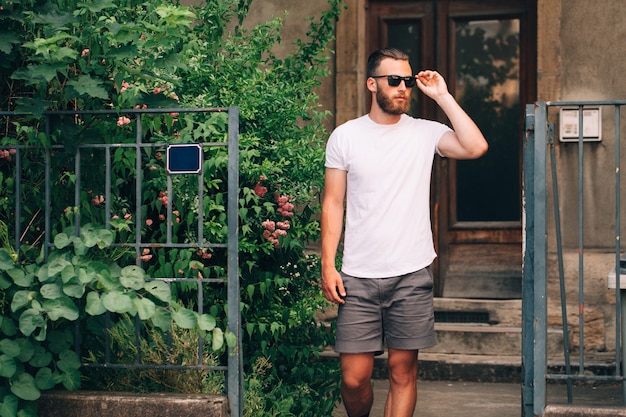 Modelo masculino guapo hipster con barba con camiseta blanca en blanco con espacio para su logotipo o diseño en estilo urbano casual