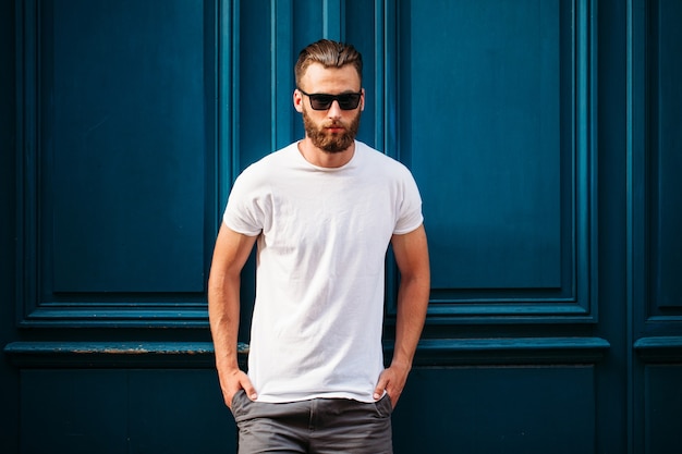 Modelo masculino guapo hipster con barba con camiseta blanca en blanco con espacio para su logotipo o diseño en estilo urbano casual