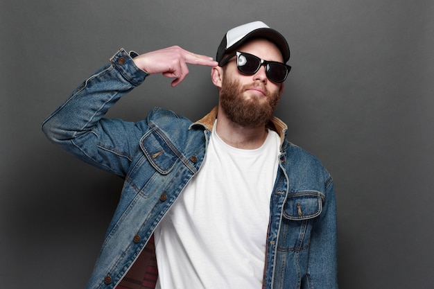 Modelo masculino guapo hipster con barba con camiseta blanca en blanco y una gorra de béisbol con espacio para su logotipo o diseño en estilo urbano casual