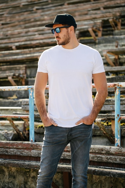 Foto modelo masculino guapo hipster con barba con camiseta blanca en blanco y una gorra de béisbol con espacio para su logotipo o diseño en estilo urbano casual