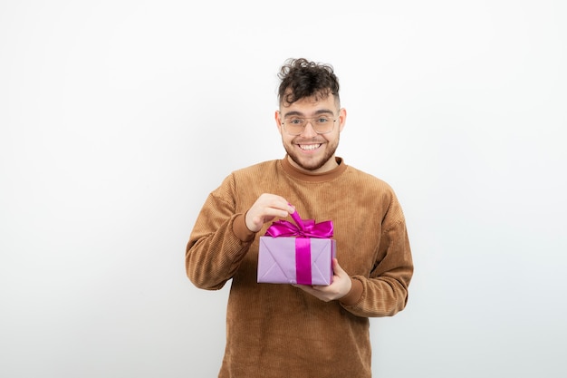 modelo masculino joven que sostiene el presente sobre la pared blanca.