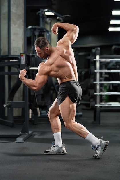 Modelo masculino musculoso doblando el cuerpo tensando los músculos en el gimnasio