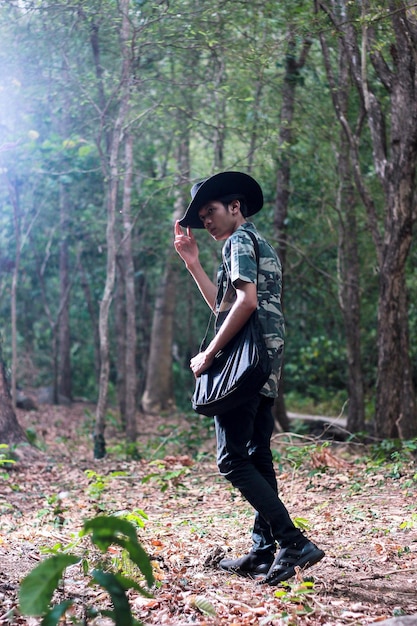 modelo masculino no meio da floresta com um chapéu em uma camisa listrada e uma bolsa preta