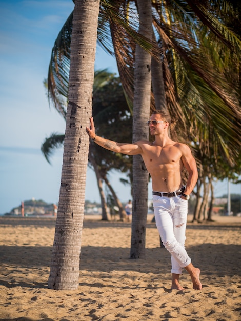 Modelo masculino en la playa. Palmeras en la hora del atardecer