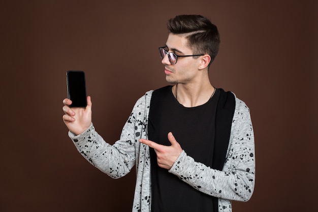 Modelo masculino que muestra el teléfono inteligente a la cámara, aislado sobre fondo marrón