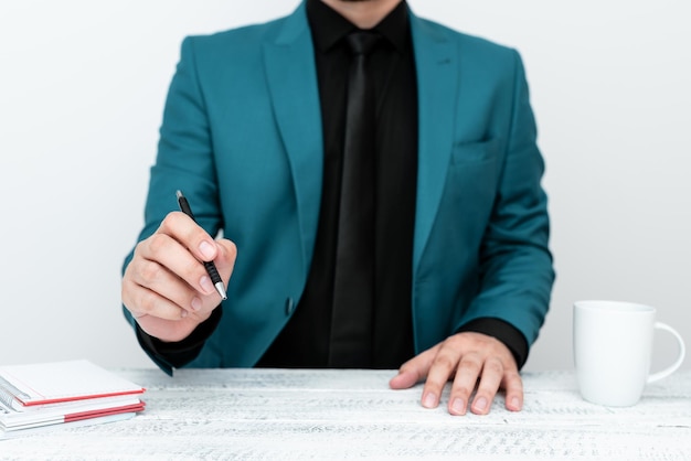 Modelo masculino en traje azul sentado en una mesa blanca y señalando con un bolígrafo en un mensaje importante Caballero mostrando un anuncio crítico Taza de café en la cubierta