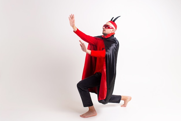 Modelo masculino en traje rojo negro de halloween y gafas de sol con sombrero y cuernos posando