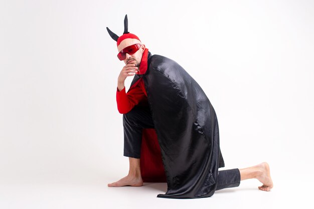 Modelo masculino en traje rojo negro de halloween y gafas de sol con sombrero y cuernos posando