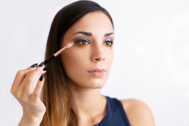 Foto modelo de moda aplicando maquillaje contra un fondo blanco