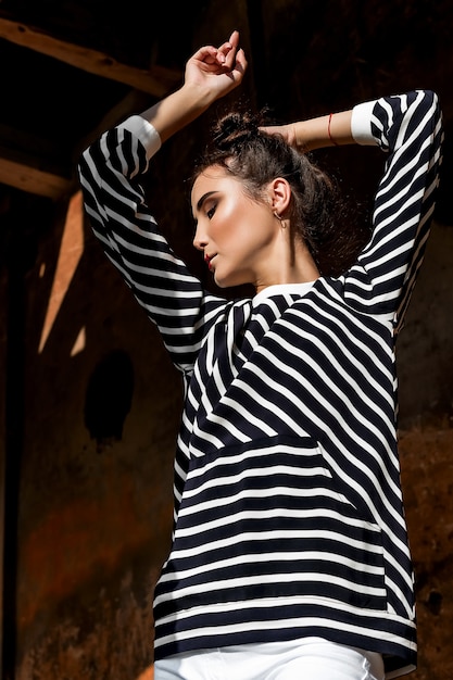 Modelo de moda de belleza Girl con cabello castaño sobre un fondo de un edificio antiguo y abandonado, vistiendo ropa elegante.