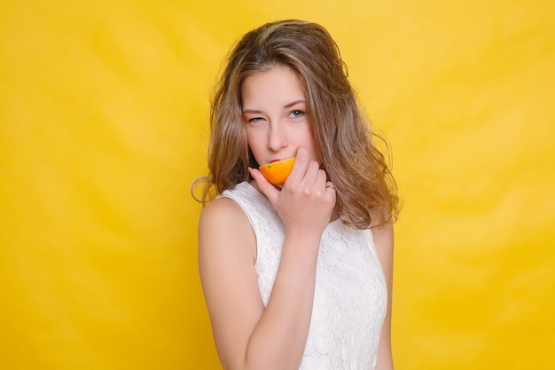 Modelo de moda divertido hermoso joven con una rodaja de naranja sobre fondo naranja. con maquillaje y peinado. sosteniendo limón con bonita sonrisa.