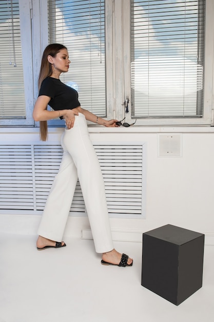 Modelo de moda hermosa joven elegante exitosa chica con ropa cómoda posando junto a la ventana con persianas. Foto de alta calidad