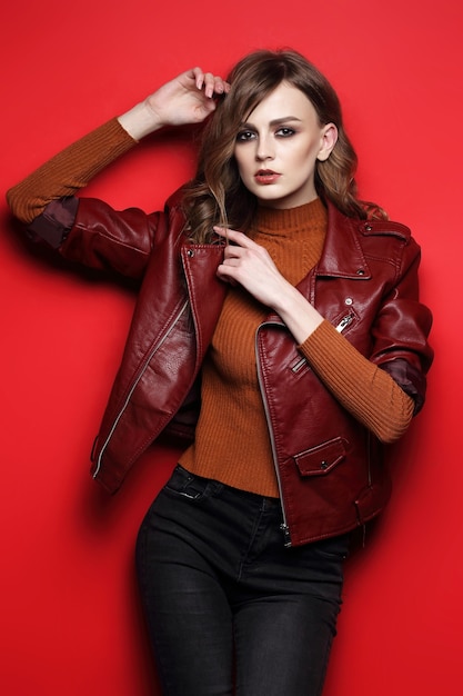 Modelo de moda hermosa mujer joven. chaqueta de cuero, tiro del estudio, fondo rojo