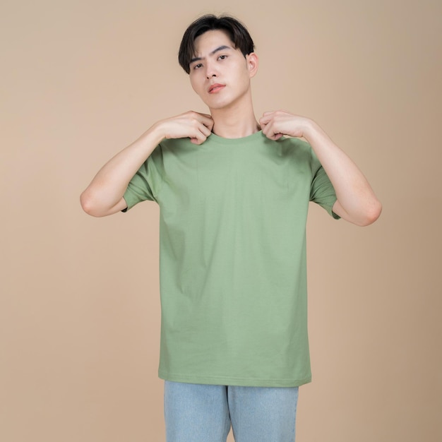 Modelo de moda masculino en camiseta verde y jeans de pie en estudio sobre fondo beige