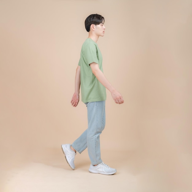 Modelo de moda masculino en camiseta verde y jeans de pie en estudio sobre fondo beige