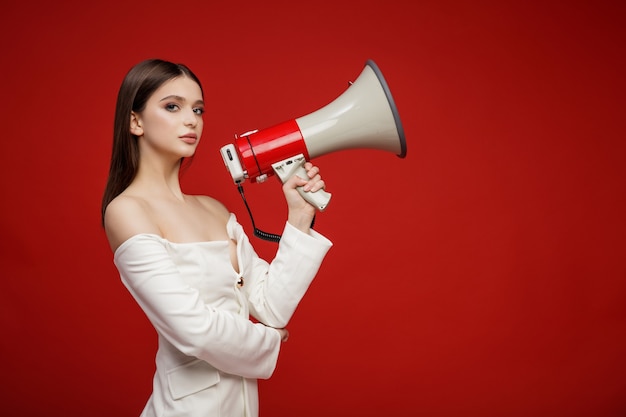 Modelo de moda con megáfono en traje blanco hermosa mujer joven Foto de estudio Fondo rojo