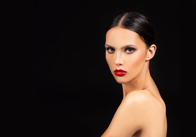 Modelo de moda morena con ojos ahumados y maquillaje de labios rojos sobre fondo negro