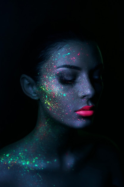 Modelo de moda mujer en luz de neón brillante fluorescente maquillaje y gotas en la cara.