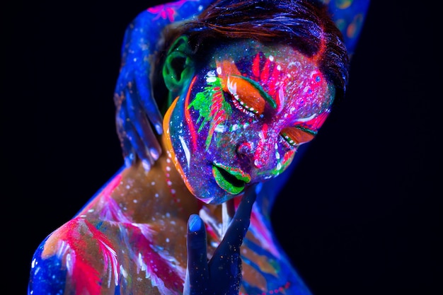 Modelo de moda mujer en luz de neón, retrato de niña hermosa modelo con maquillaje fluorescente, Body Art en UV, cara pintada, maquillaje colorido, sobre fondo negro