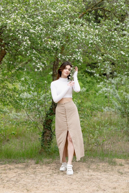 Modelo de moda posando en un parque floreciente tocando la rama de un árbol mirando a la cámara