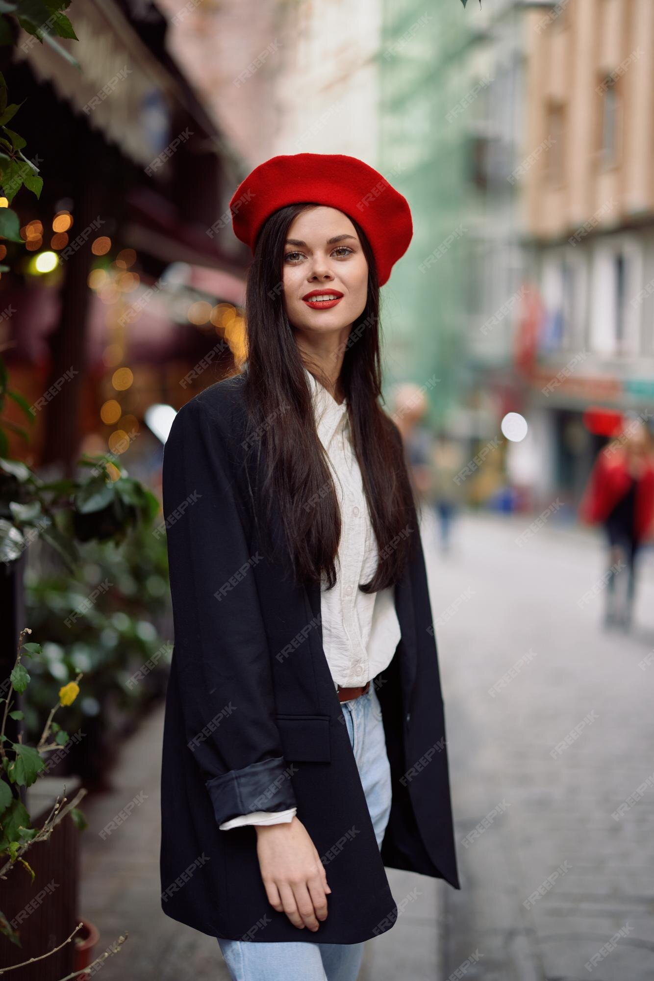 de moda de sonrisa mujer camina en en el centro de la ciudad entre la multitud en una chaqueta y boina roja y jeans ropa de estilo de