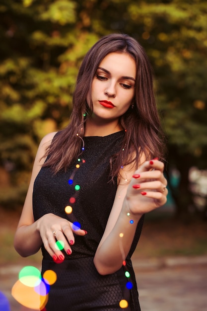 Modelo morena de lujo con maquillaje brillante con guirnalda en el parque de la ciudad