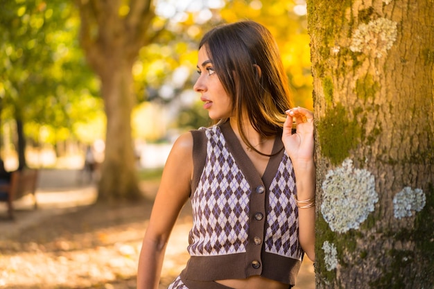 Modelo morena en otoño al atardecer en un parque natural de la ciudad junto a un árbol