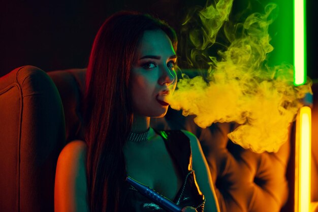 Modelo morena sexy está fumando una pipa de agua exhalando un humo en un club nocturno de lujo.