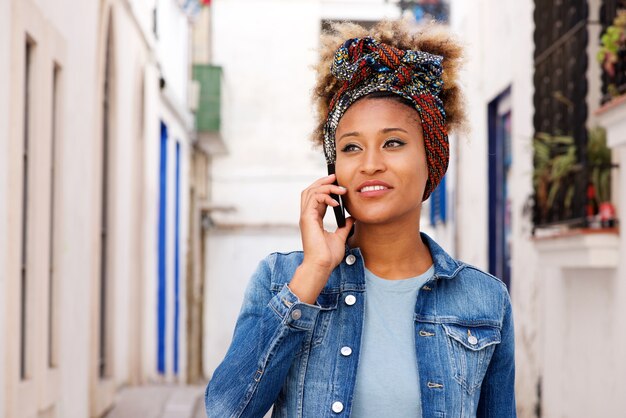 Modelo de mujer africana caminando en la calle y hablando por teléfono inteligente