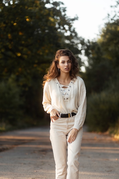 Modelo de mujer bonita con peinado rizado en un suéter de punto de moda camina en el parque en la naturaleza