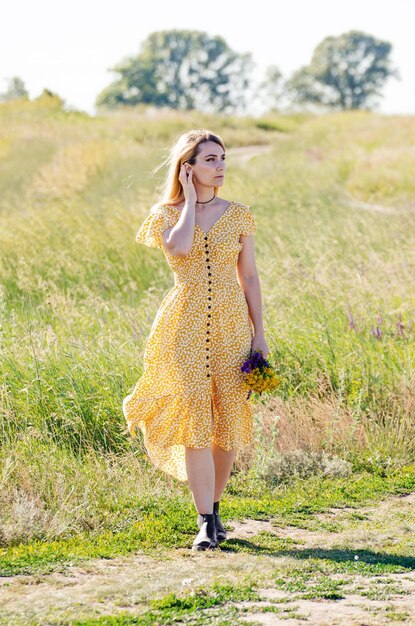 Modelo de mujer caucásica rubia joven con flores en la mano caminar día soleado de verano al aire libre.