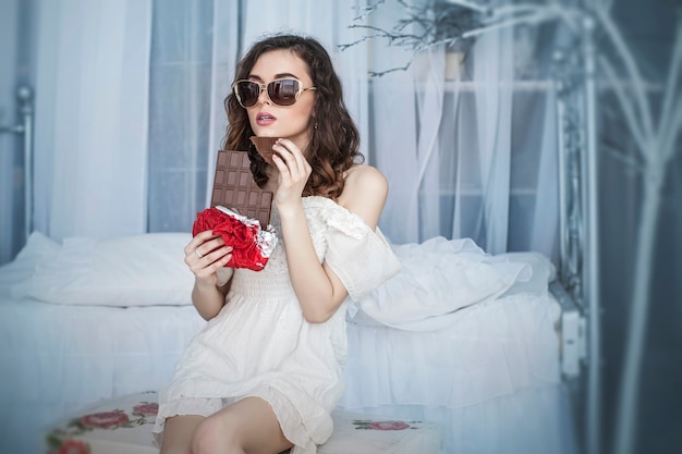 Modelo de mujer hermosa con azulejos de chocolate negro en las manos contra el interior del dormitorio