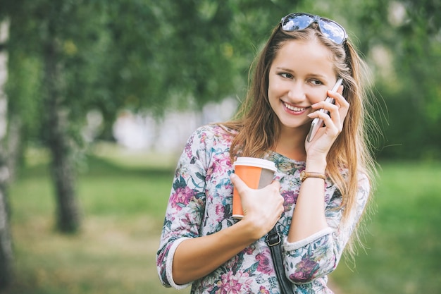 Modelo de mujer hermosa con café para llevar y un teléfono en el parque
