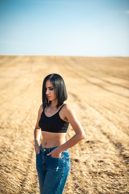 Modelo de mujer hermosa con ropa de algodón de verano posando en el campo de otoño con pila de heno